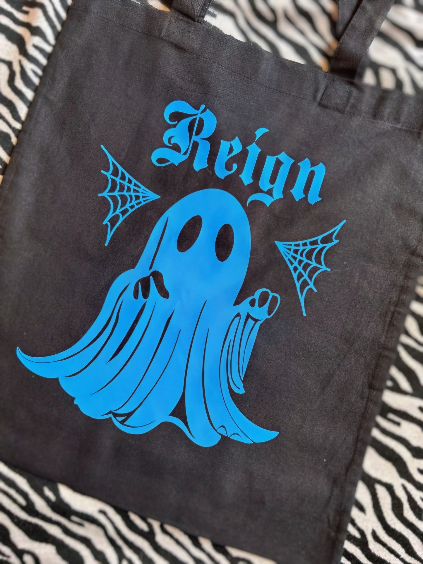A tote bag, black with a print of a ghost, in blue with a name. This is an example of a customisation.