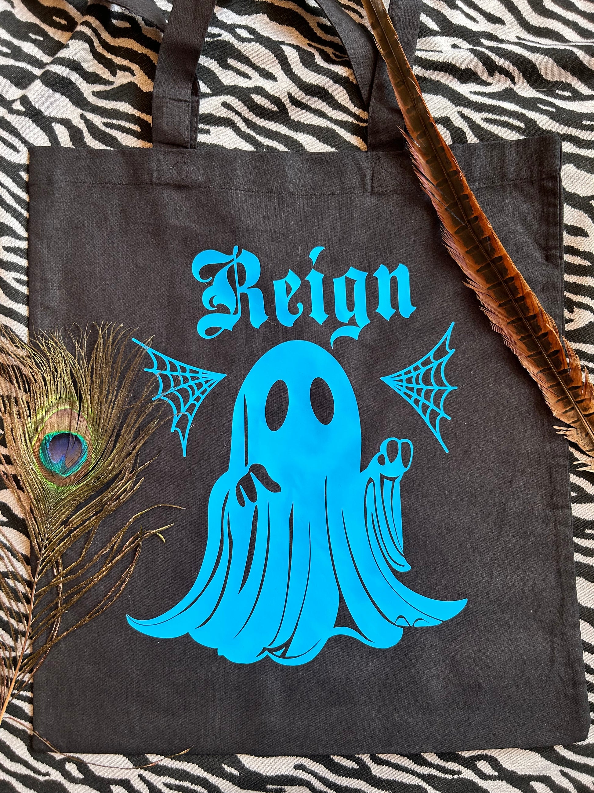 A tote bag, black with a print of a ghost, in blue with a name. This is an example of a customisation.